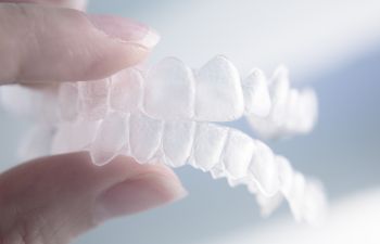 A person holding a set of clear aligners with their fingers.