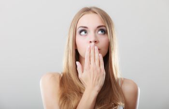 A woman covering her mouth because of halitosis.