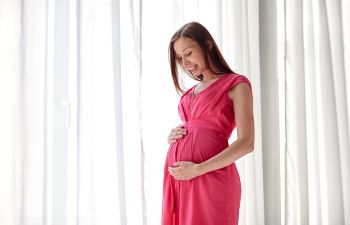 A broadly smiling pregnant woman with nice teeth holding her belly.