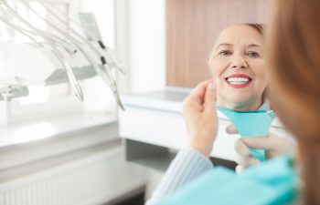 A mature woman after dental restorative treatment looking at her teeth in the mirror.