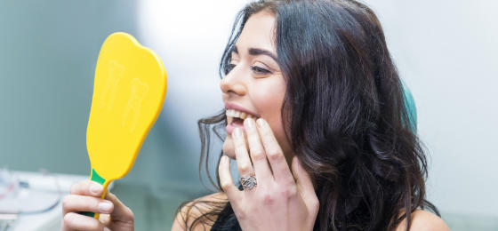 Happy woman after dental treatment looking at her teeth in the mirror.