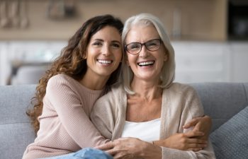 Portrait of two beautiful young and mature females, different generations women hugging sit on sofa, sharing warmth, joyful moments together. Family ties, intergenerational connection, love, support