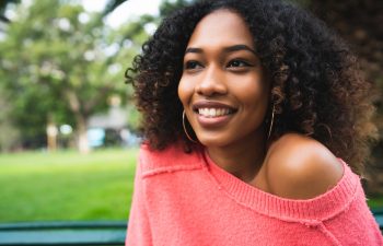 Portrait of young beautiful afro american woman sitting on bench in the park. Outdoors.